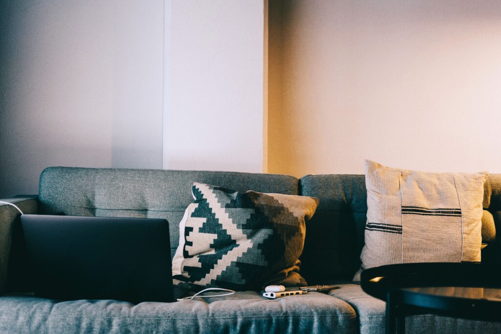 A cozy living room setup featuring a sofa with pillows and a laptop, perfect for relaxation and remote work.