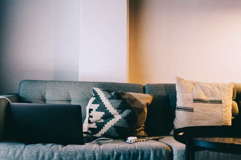 A cozy living room setup featuring a sofa with pillows and a laptop, perfect for relaxation and remote work.