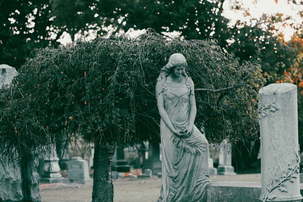 A tranquil stone statue amid lush greenery in a cemetery, evoking a sense of serenity.