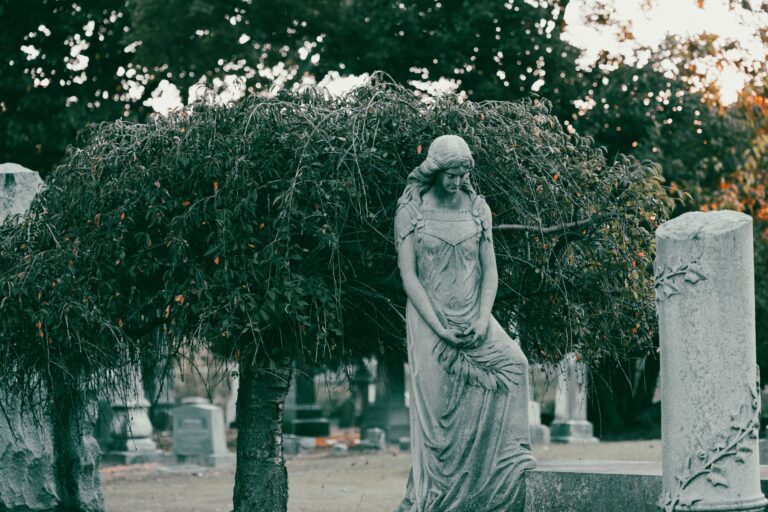 A tranquil stone statue amid lush greenery in a cemetery, evoking a sense of serenity.